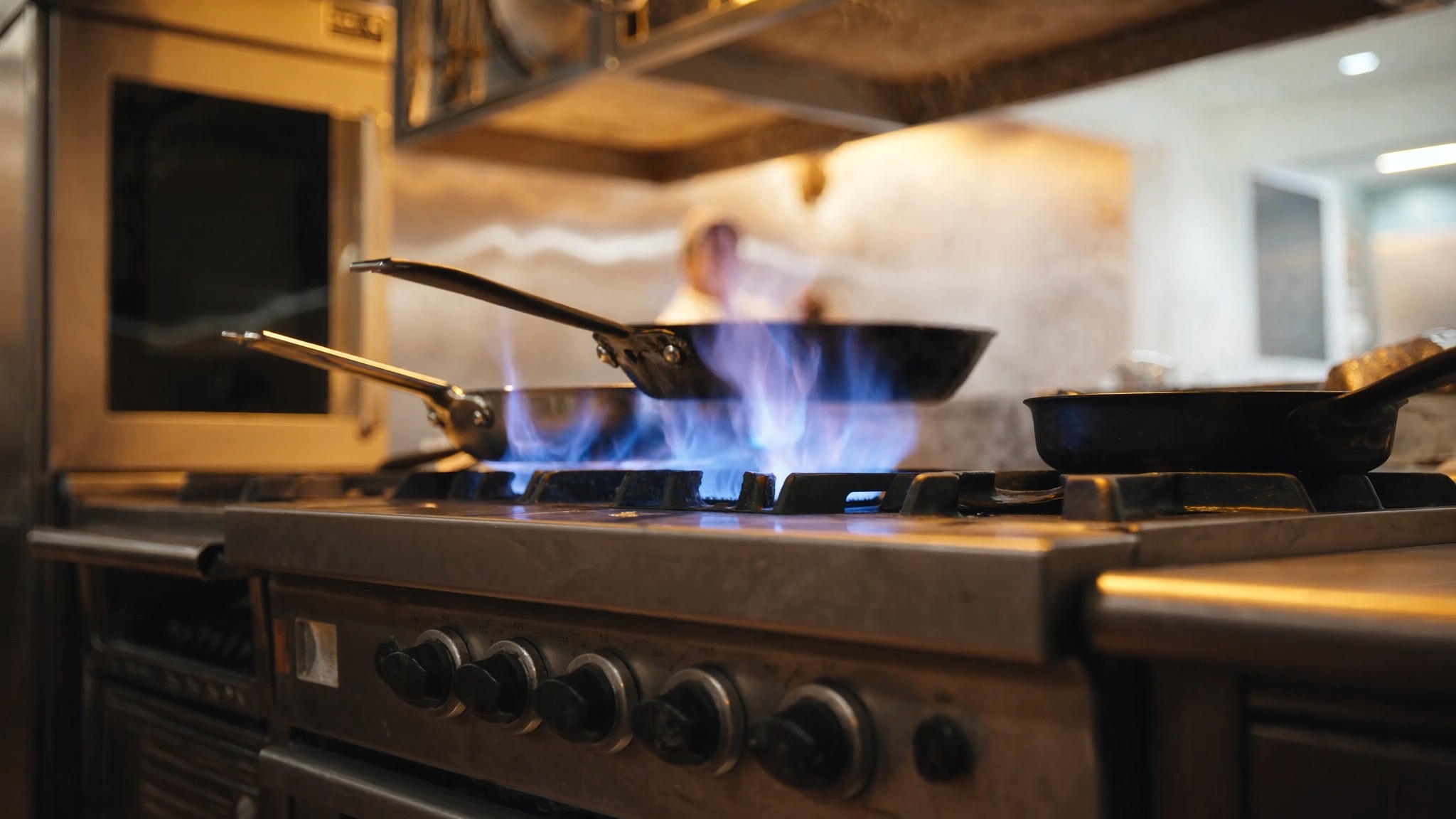 A commercial kitchen range burning blue propane flame under a sauté pan